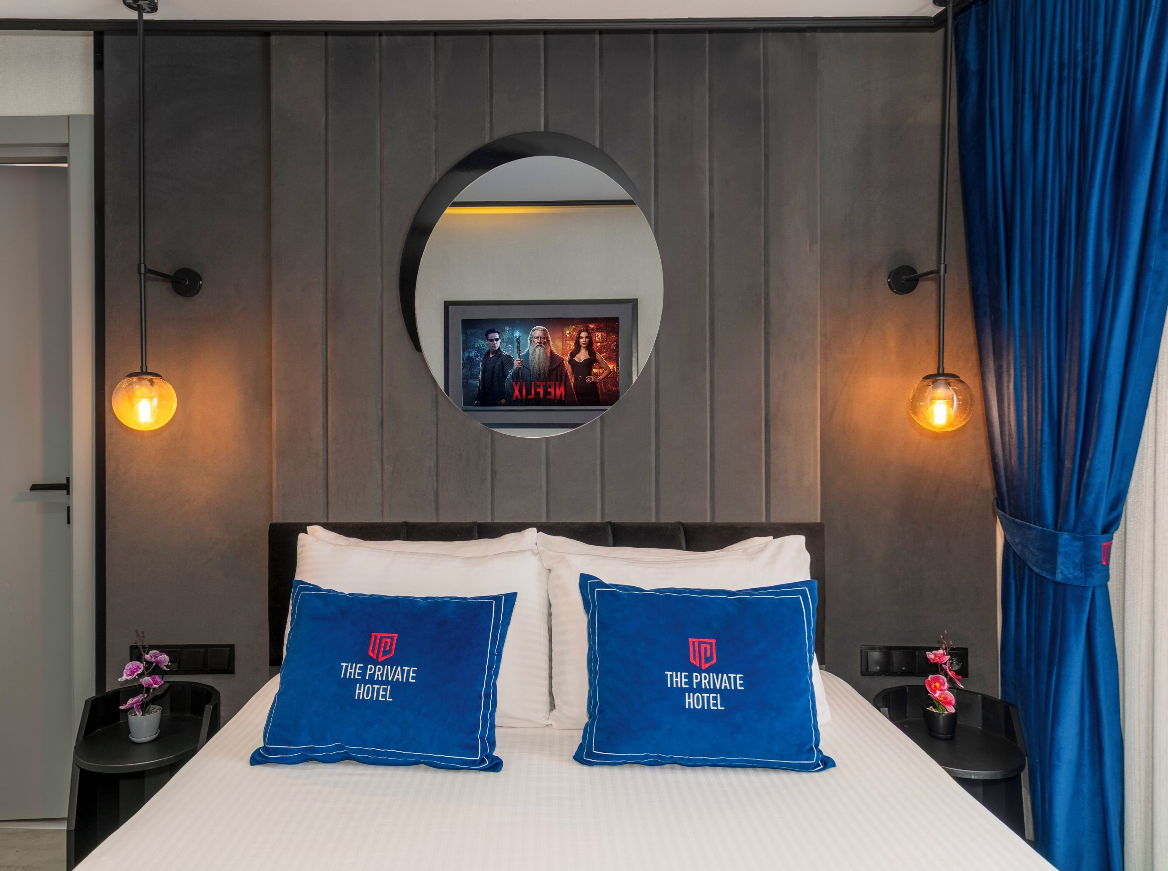 A hotel room with a bed, two pillows with the hotel's logo, a TV on the wall, and two bedside lamps.
