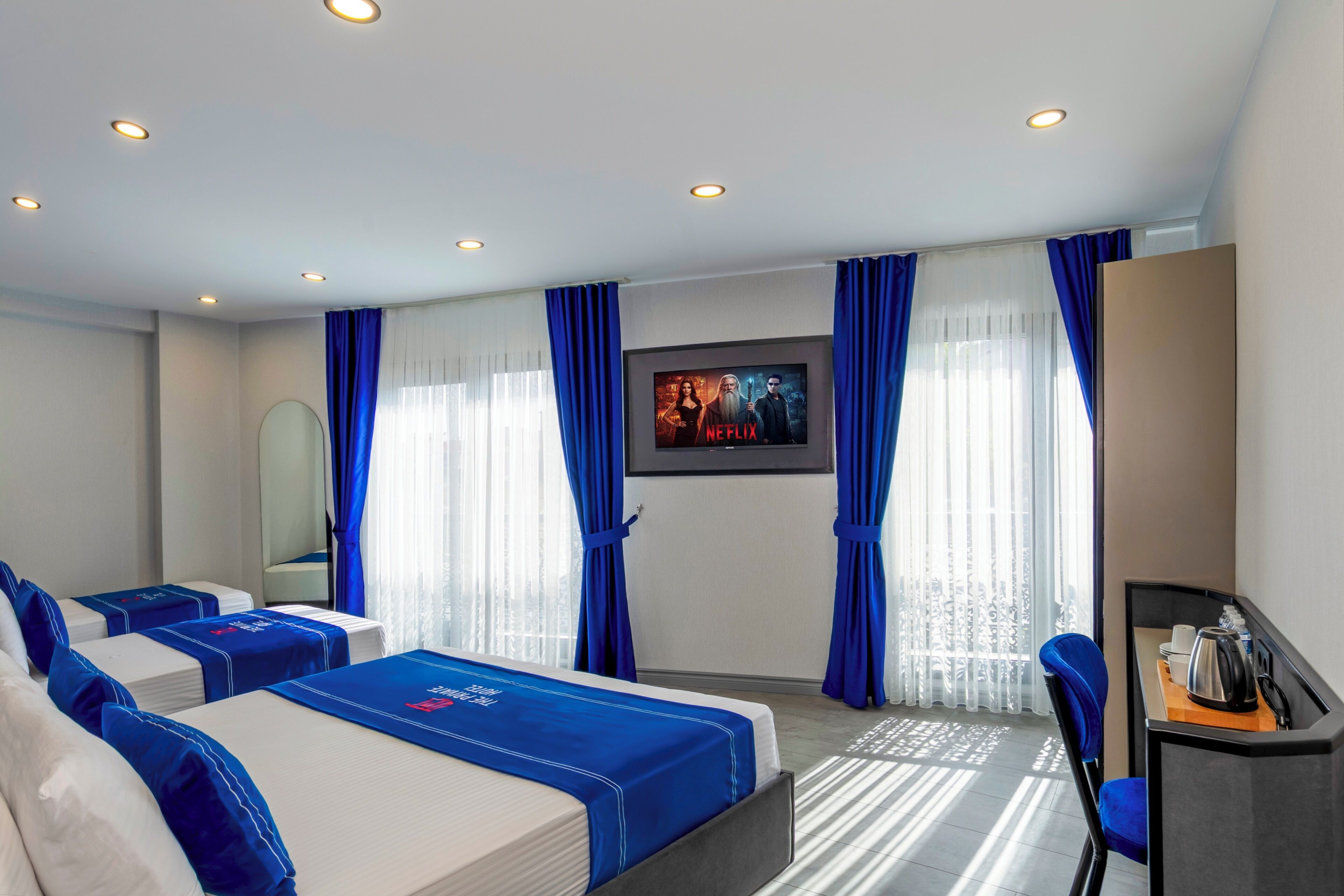 A hotel room with two beds, a desk, a chair, a TV, and a window with curtains.