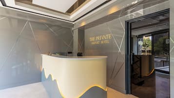 A reception desk with a modern design, a glass door entrance, and the text "THE PRIVATE AIRPORT HOTEL" on the wall.