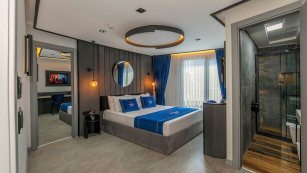 Ein modernes Hotelzimmer mit einem großen Bett, einem runden Spiegel, einem Fernseher und einer Duschkabine aus Glas.