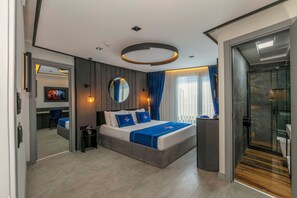 A modern hotel room with a large bed, a round mirror, a TV, and a glass-enclosed shower. - The Private Airport Hotel (Arnavutköy)