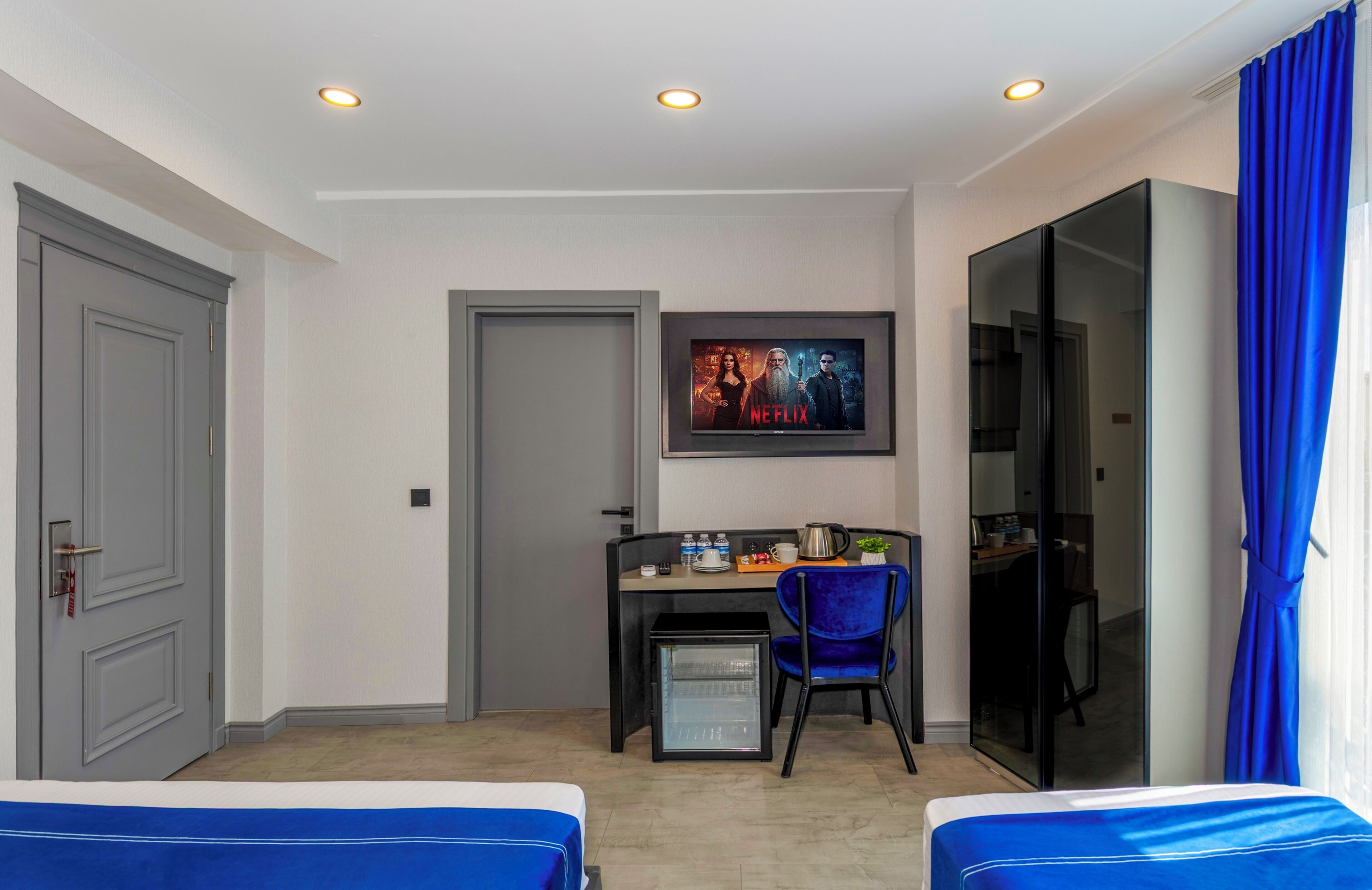A hotel room with two beds, a desk with a computer, a TV, and a minibar.