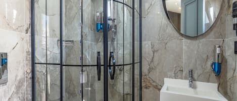 A modern bathroom with a glass-enclosed shower, a round mirror, and a white sink.
