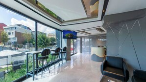Eine moderne Hotelhalle mit einem großen Glasfenster, einer Sitzecke mit Stühlen und einem Tisch sowie einer Rezeption.