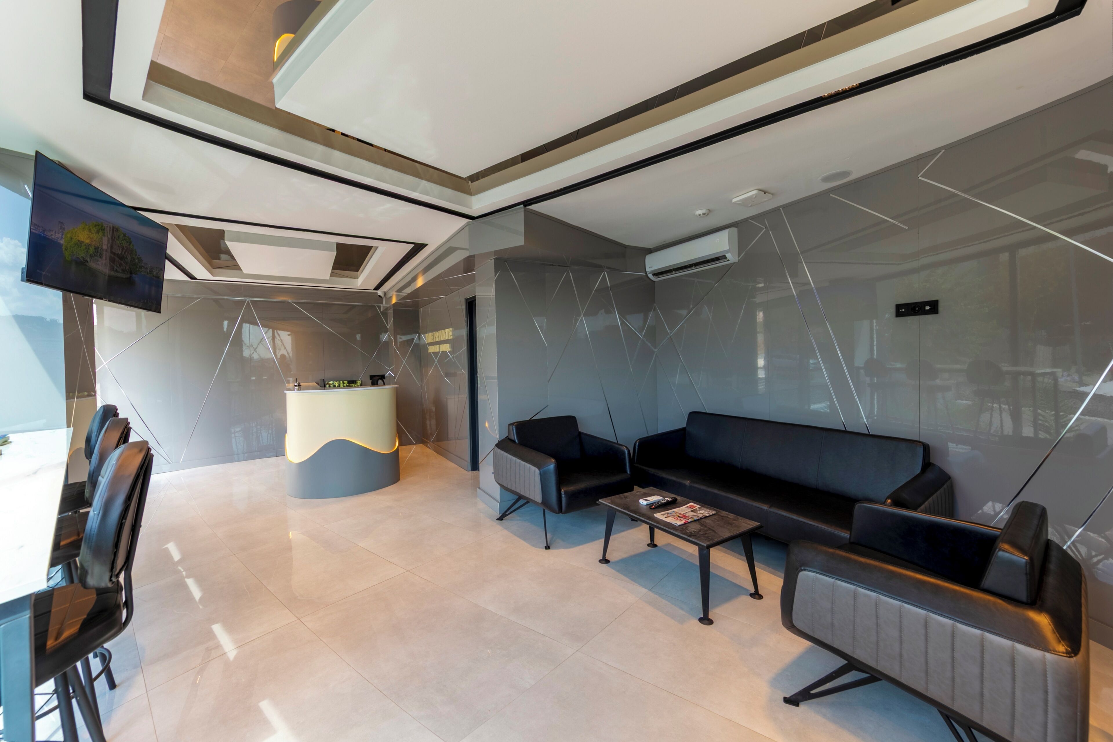 A modern hotel lobby with a reception desk, seating area, and a large flat-screen TV.