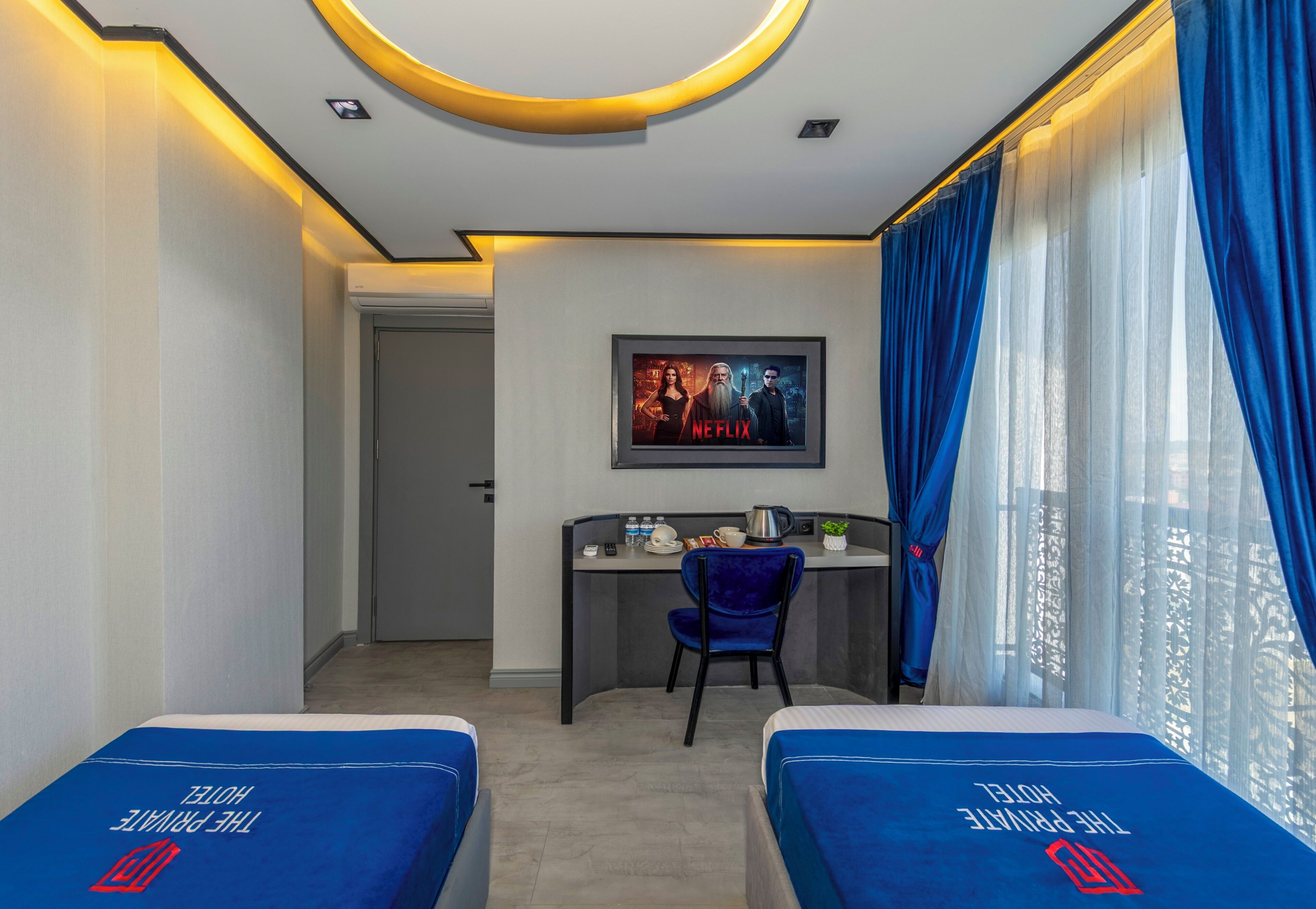 A hotel room with two beds, a desk, a chair, and a large window with curtains.