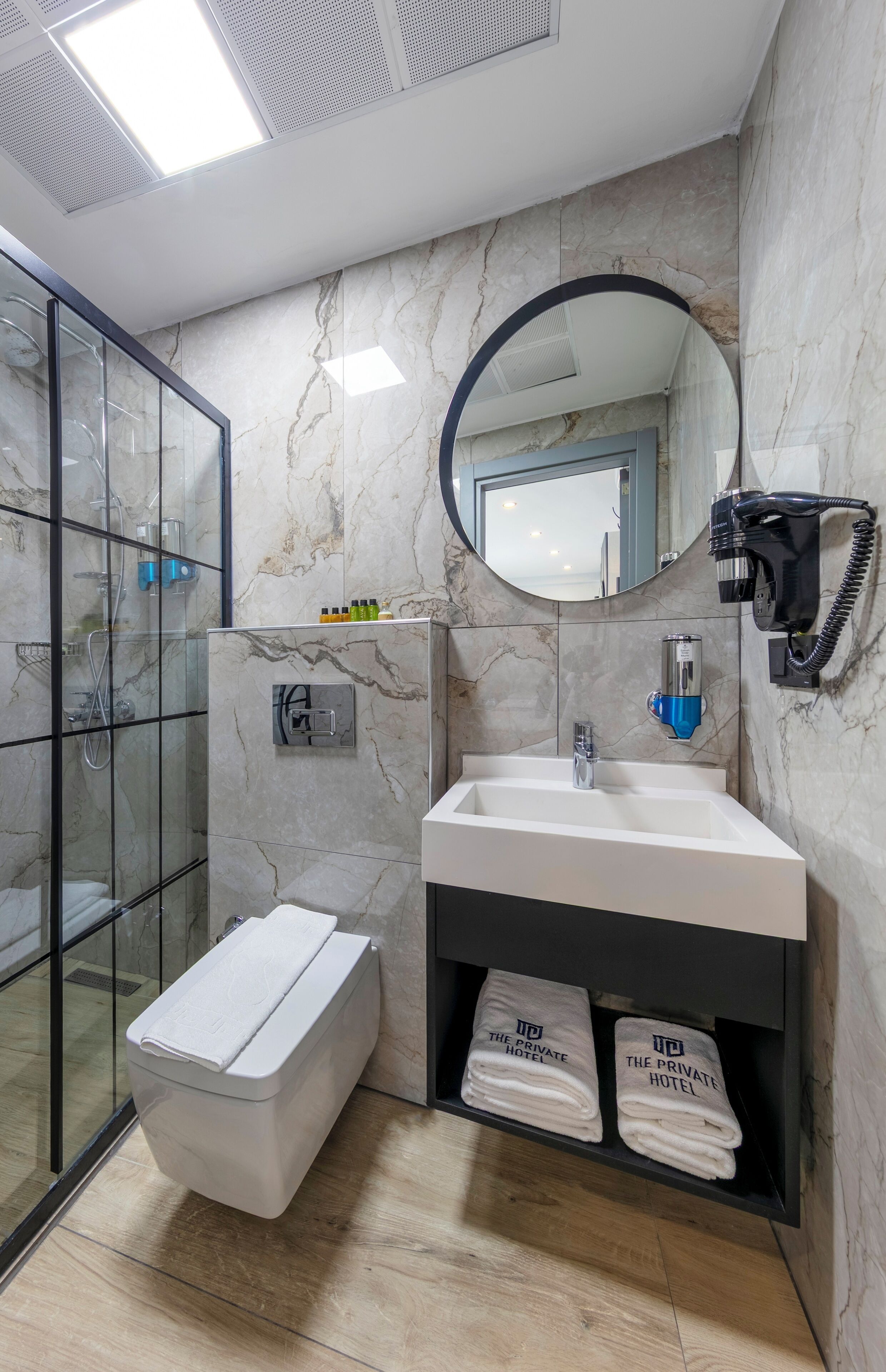 A modern bathroom with a glass shower enclosure, a white sink, a mirror, and a towel rack.