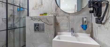 A modern bathroom with a glass shower enclosure, a white sink, a mirror, and a towel rack.
