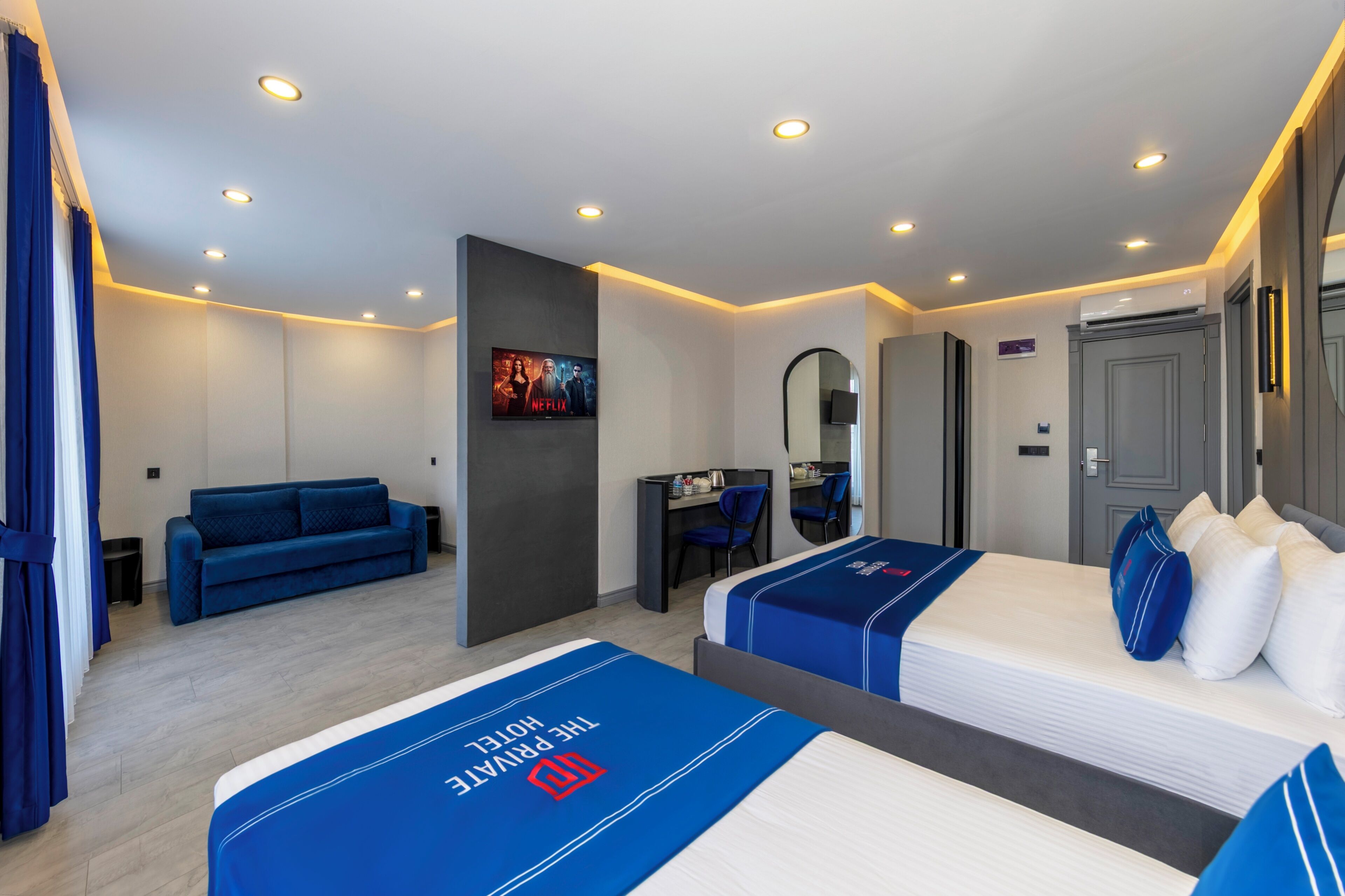 A hotel room with a bed, a sofa, a desk, and a mirror.