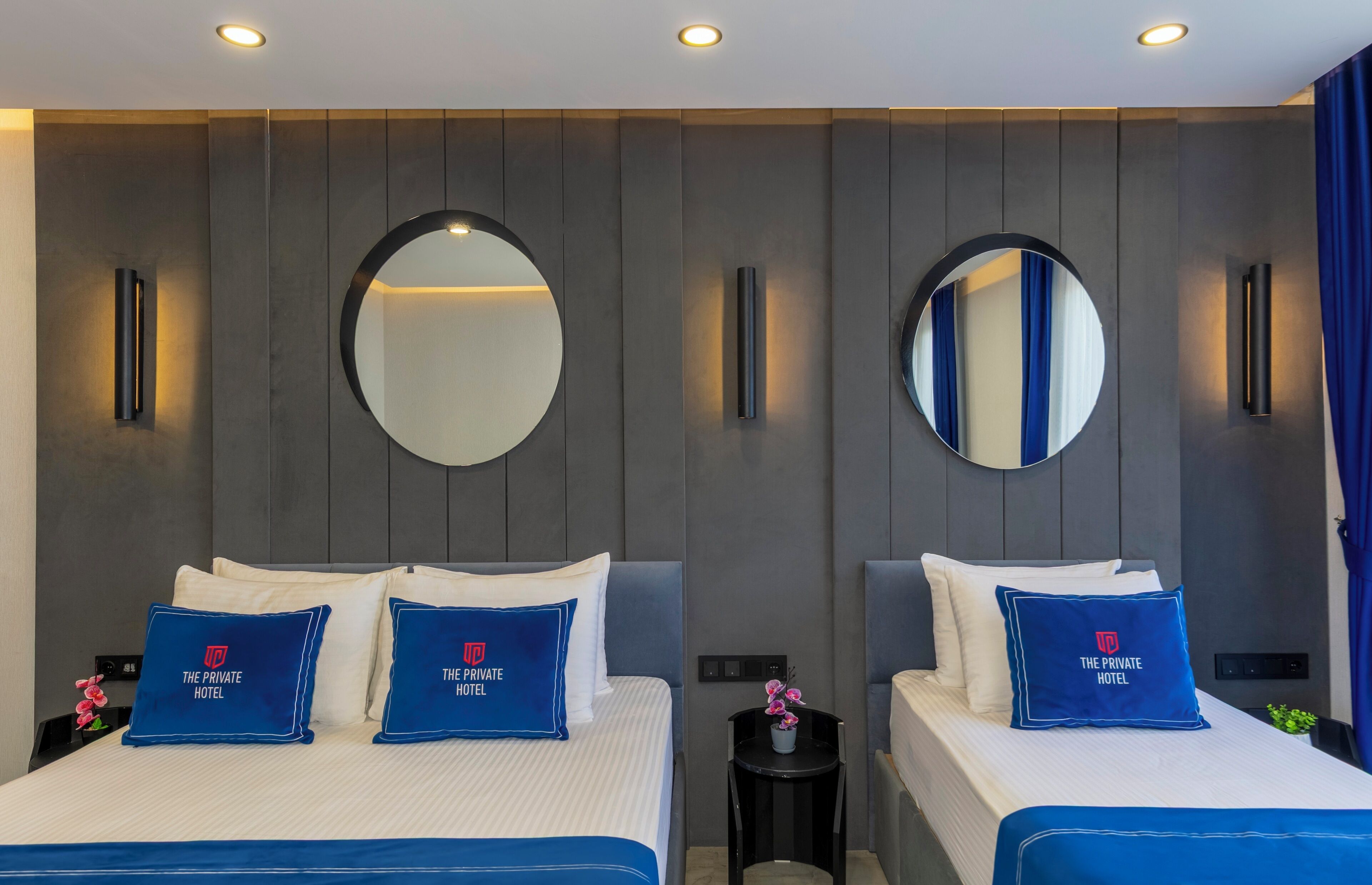 Ein Hotelzimmer mit zwei Betten, jedes mit einem blauen Kissen und einem Spiegel darüber.