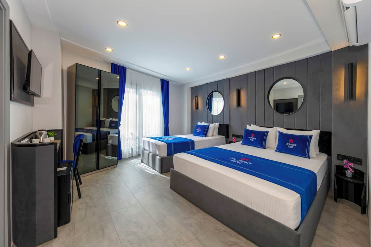 A modern hotel room with a large bed, a desk, a chair, a mirror, and a view of the city.