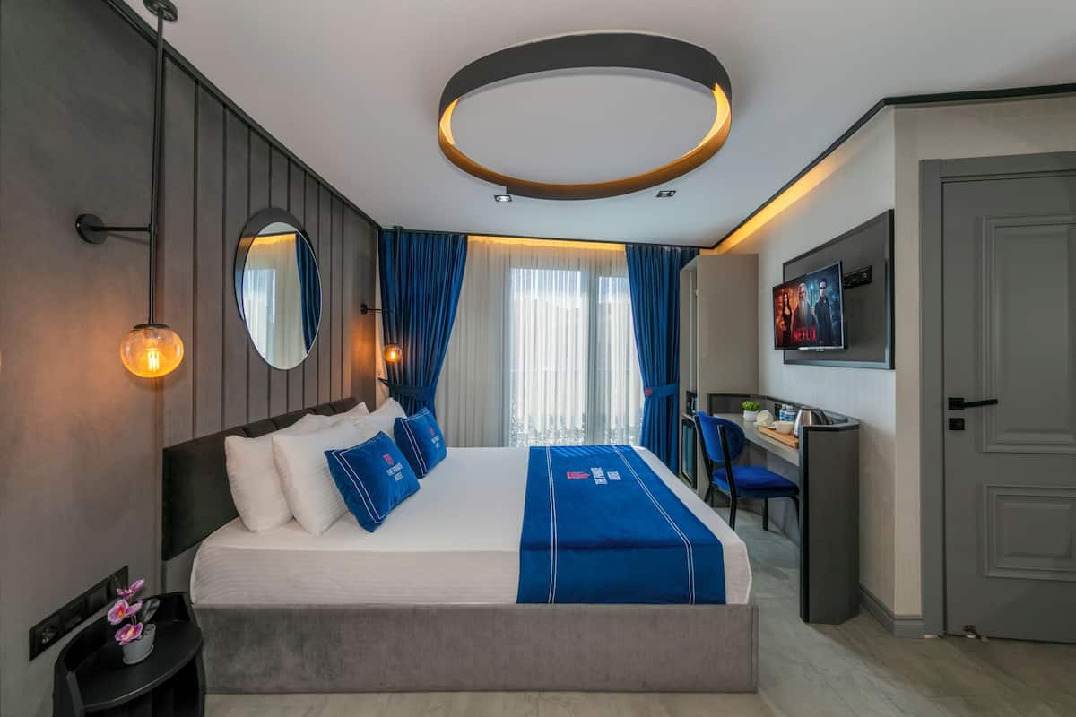 A modern hotel room with a large bed, a desk, and a TV on the wall.