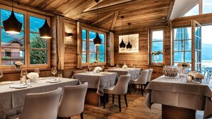 A wooden interior with tables set for dining, large windows, and hanging pendant lights. - Appartment mit Balkon und Seeblick (Grundlsee)
