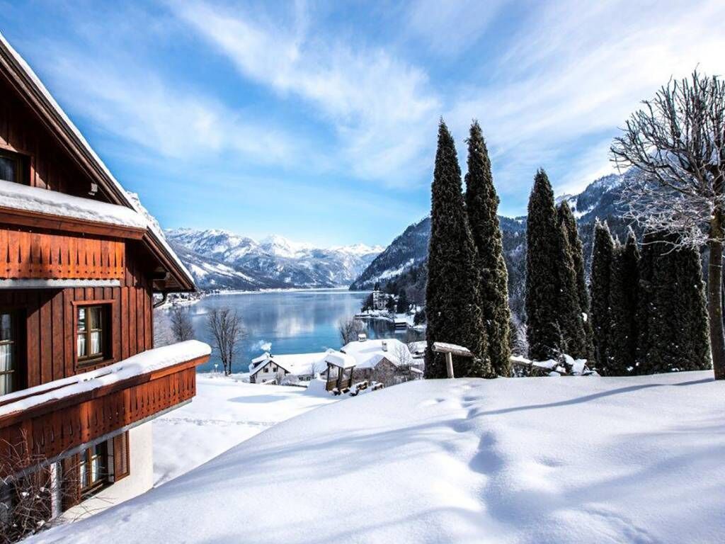 Una baita di legno con un balcone che si affaccia su un paesaggio innevato e un lago.