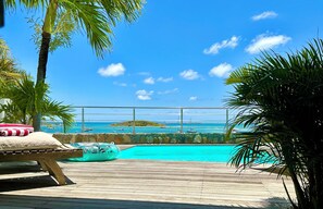 Une terrasse en bois avec une piscine, des palmiers et une vue sur l’océan.