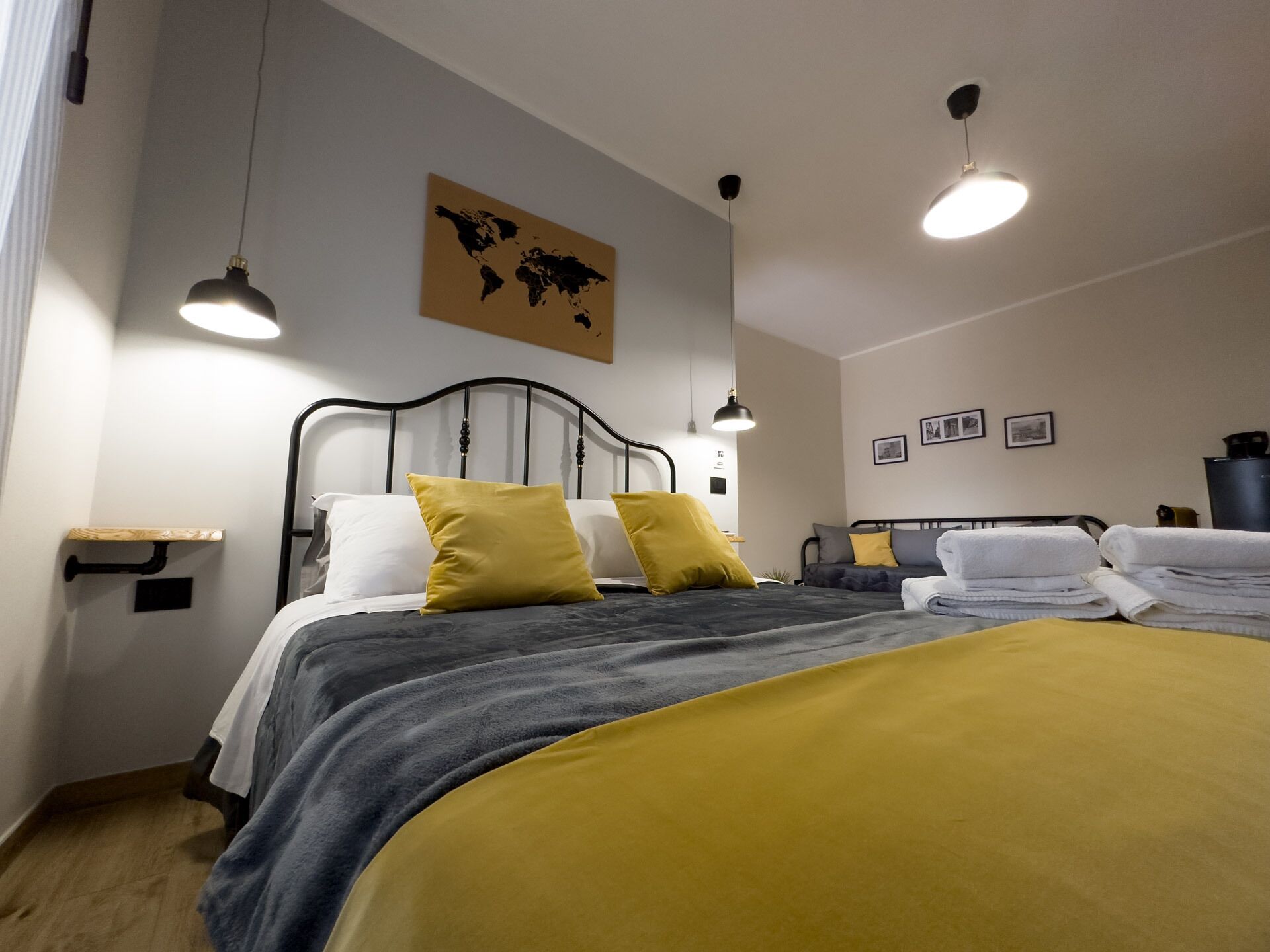 A neatly arranged bedroom with a bed, bedside lamps, a world map on the wall, and a small shelf.
