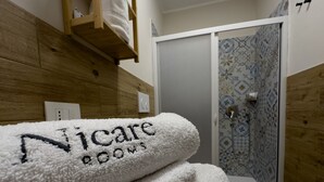 Une salle de bain avec un mur en bois, une serviette blanche ornée d’une broderie « Niche Rooms », et une douche avec des carreaux à motifs.