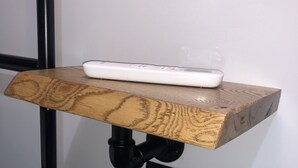 Une étagère en bois sur laquelle repose un appareil électronique blanc, le tout fixé au mur à l’aide d’un tuyau noir.