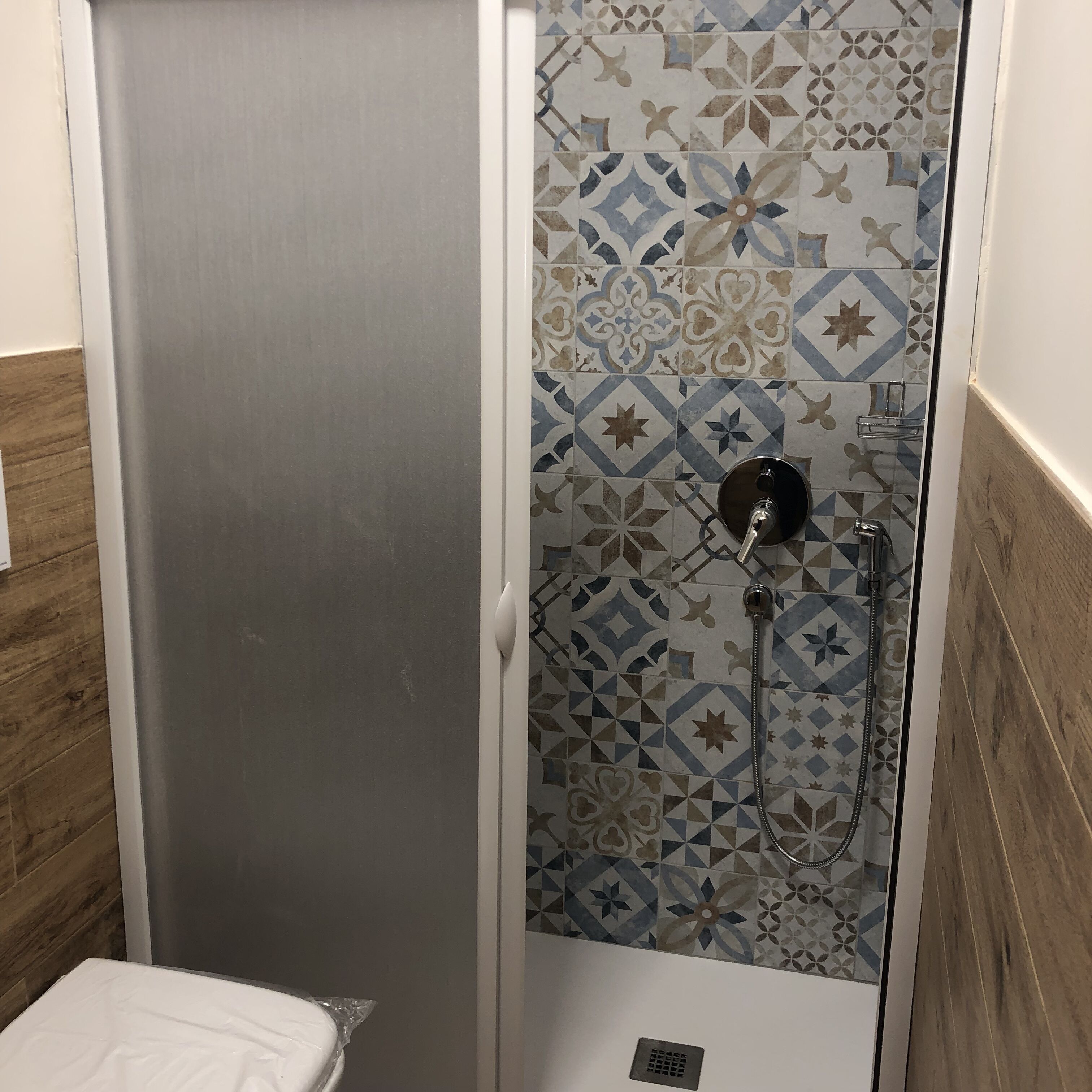 A shower enclosure with a patterned tile wall, a white door, and a metal showerhead.