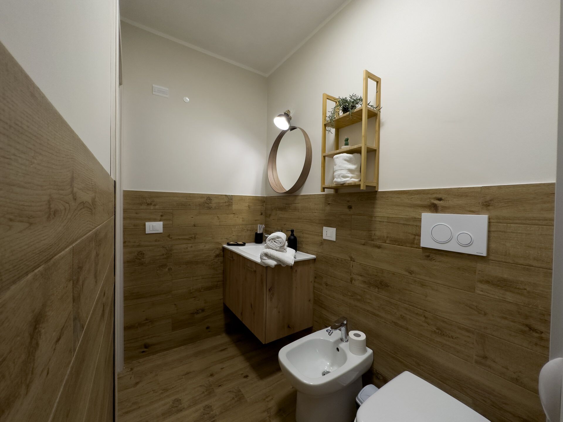 Un baño moderno con paneles de madera, un mueble de tocador de madera, un lavamanos, un bidé y un inodoro.