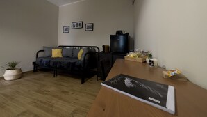Un espace de vie compact comprenant un canapé, une petite table, une plante en pot et un réfrigérateur.