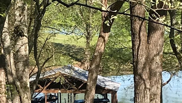 A rustic wooden structure with a roof, surrounded by trees and a body of water. - Nashville/Old Hickory Lake cottage (Mt. Juliet)