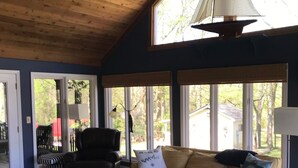 A spacious living room with a high ceiling, a ceiling fan, a large window, a sofa, a coffee table, and a patterned rug. - Nashville/Old Hickory Lake cottage (Mt. Juliet)