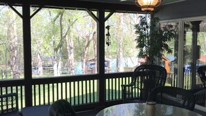 A covered outdoor seating area with a round table and wicker chairs, a ceiling fan, and a view of trees and a fence. - Nashville/Old Hickory Lake cottage (Mt. Juliet)