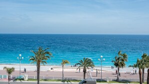 A coastal promenade with palm trees, a beach, and a clear blue sky. - Happyfew Palazzo del sol (Nice)