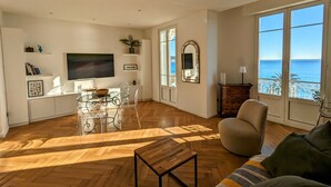 A spacious living room with a wooden herringbone floor, a glass dining table, and a comfortable sofa. - Happyfew Palazzo del sol (Nice)