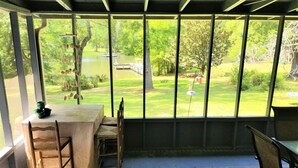 A conservatory with a table and chairs, a view of a pond and greenery outside.
