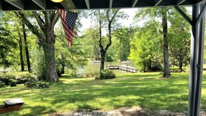 A covered patio area with a view of a pond, surrounded by trees and a dock.