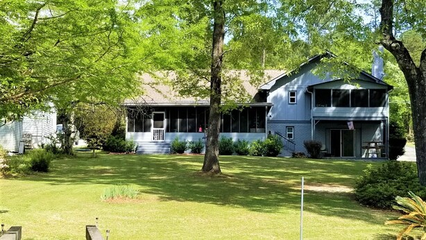 A two-story house with a front porch, a small deck, and a pond in the foreground.