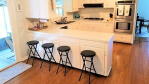A modern kitchen with white cabinetry, a central island with stools, stainless steel appliances, and a view of the dining area.