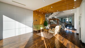 Un vaste espace de vie doté d’un plancher en bois, d’un canapé vert, d’une table basse et d’un escalier menant à un niveau supérieur.