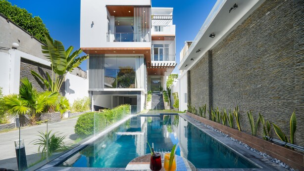 Un espace piscine moderne avec une table en verre, deux boissons et une vue sur un immeuble à plusieurs étages.