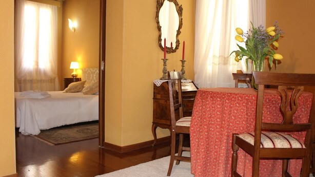 Una habitación de hotel con una cama, una mesa de comedor con sillas, un espejo y un jarrón con flores.