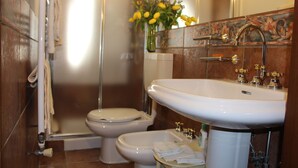 Un baño con un lavamanos blanco, dos inodoros, una ducha y un florero con flores amarillas.