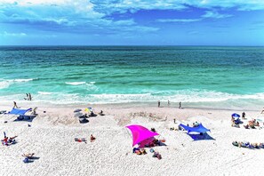 En strand med vit sand, kristallklart turkost vatten och människor som solar.