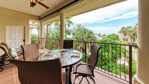 A covered outdoor patio with wicker furniture, a ceiling fan, and a view of palm trees and buildings. - La Casa Marie - 3 Bedroom Luxury Condo in Beachfront Complex - Anna Maria - By I (Holmes Beach)