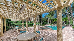 A covered outdoor area with a pool, seating, and a pergola structure. - La Casa Marie - 3 Bedroom Luxury Condo in Beachfront Complex - Anna Maria - By I (Holmes Beach)