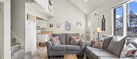 A modern living room with a grey sofa set, a wooden coffee table, and a view of a park through large windows.
