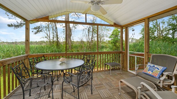 Une terrasse extérieure couverte, avec une table ronde et des chaises, un ventilateur de plafond et une vue sur un champ verdoyant.