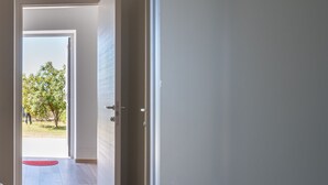 Un pasillo con piso de madera, un tapete rojo y una puerta que da a un área exterior luminosa con un árbol y una persona a lo lejos.