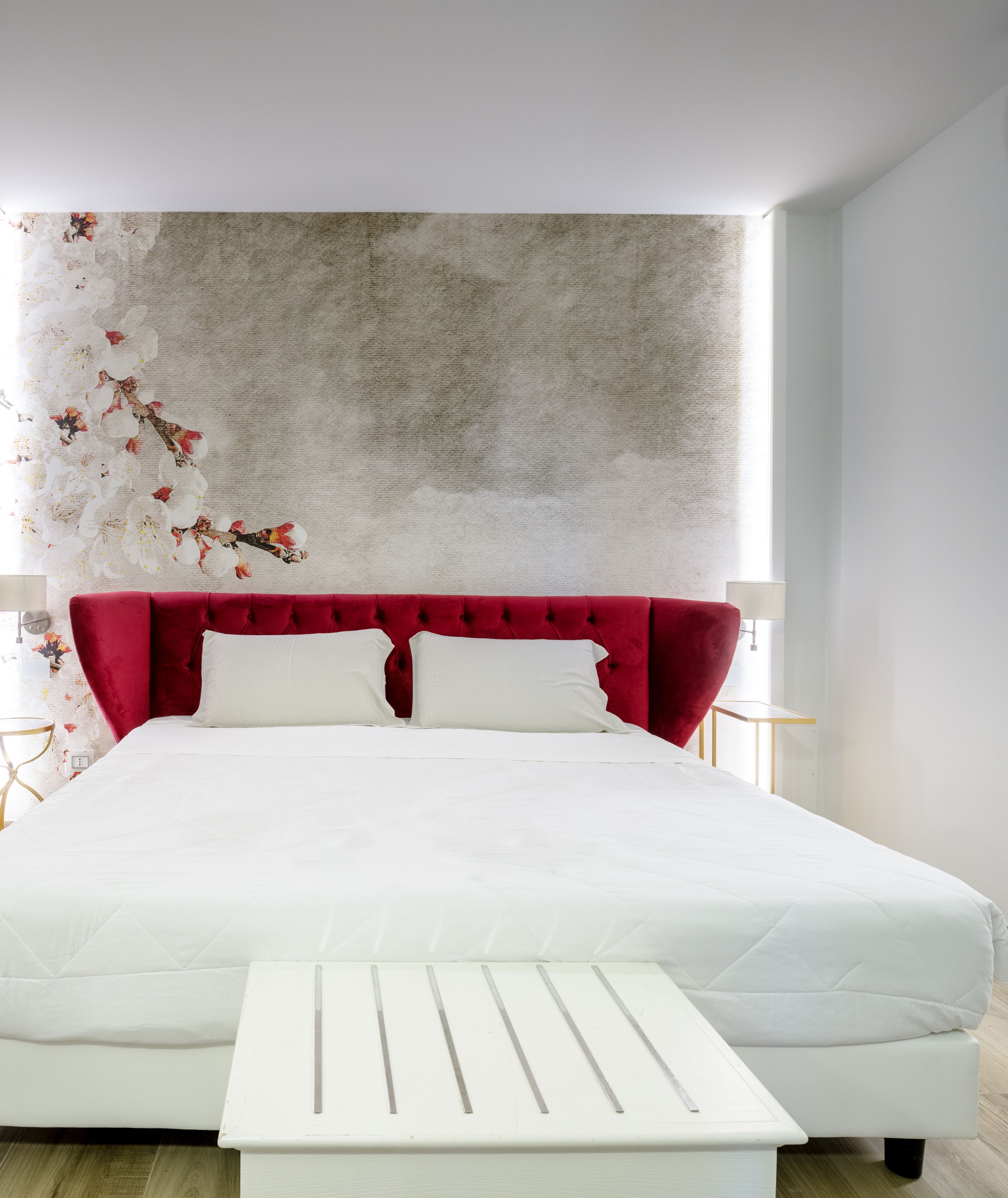 Une chambre à coucher moderne avec un grand lit, une tête de lit rouge recouverte de tissu et une table de chevet blanche.