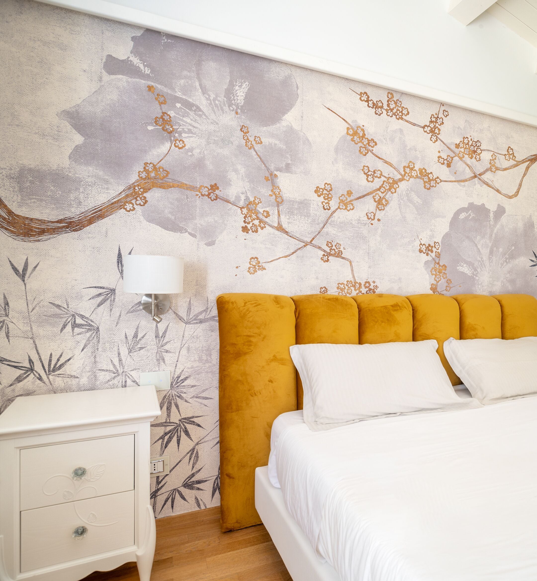 A bedroom with a bed, a nightstand, a lamp, and a wall with floral and bamboo patterns.