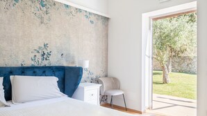 Un dormitorio con cama, una mesita de noche, una silla y vistas a un jardín a través de un ventanal.