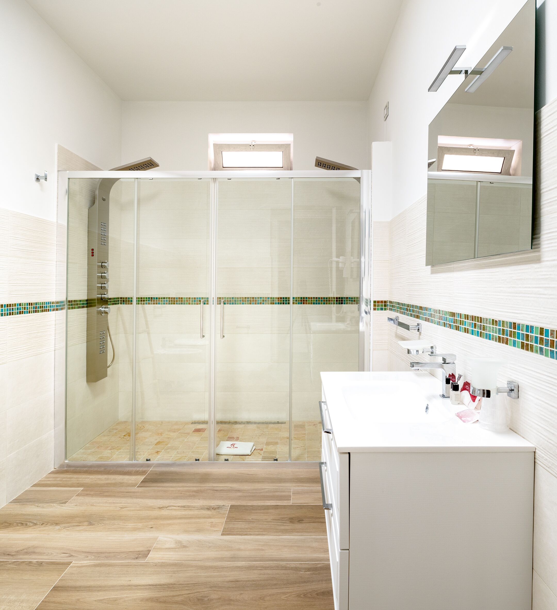 Un baño moderno con cabina de ducha de vidrio, lavamanos blanco con artículos de aseo y salpicadero de azulejos.