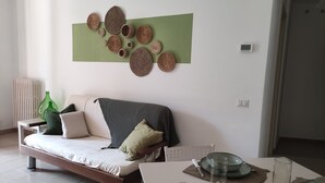Una sala moderna con un sofá, una mesa de comedor con platos y vasos, y una obra de arte abstracta de color verde en la pared.