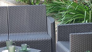 Un patio amueblado con muebles de mimbre, incluyendo un sofá y una mesita con vasos de vidrio verde.